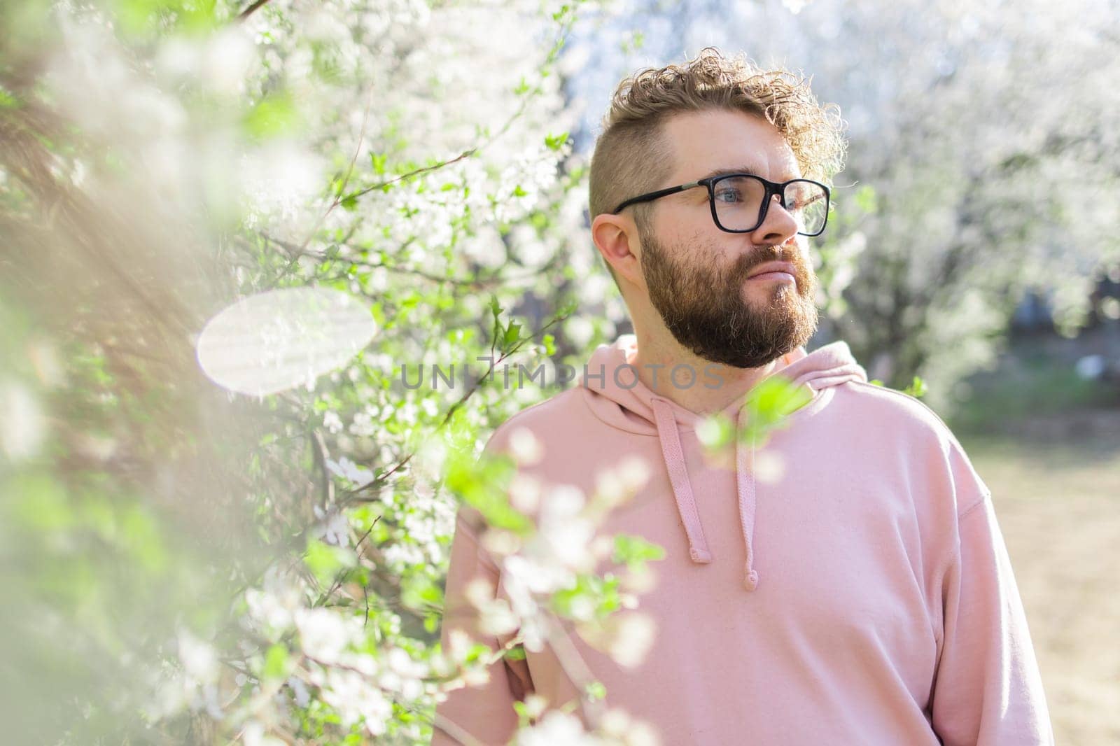 Cool handsome millennial man side face looking away portrait in blooming springtime trees. Blur sakura blossom spring tree background. Copy space by Satura86