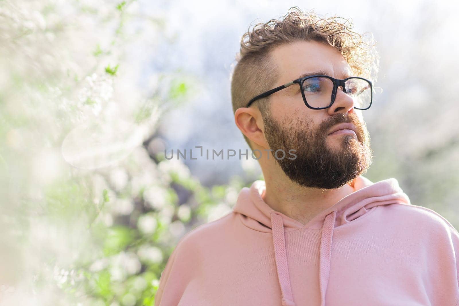 Cool handsome millennial man side face looking away portrait in blooming springtime trees. Blur sakura blossom spring tree background. Copy space by Satura86