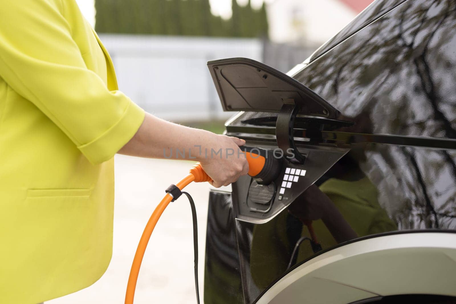 Female hand holding electric car plug for recharge plug in hybrid car at home or charging station. World Environment Day. Save world save life. Woman's hands plugging in her electric car to charge