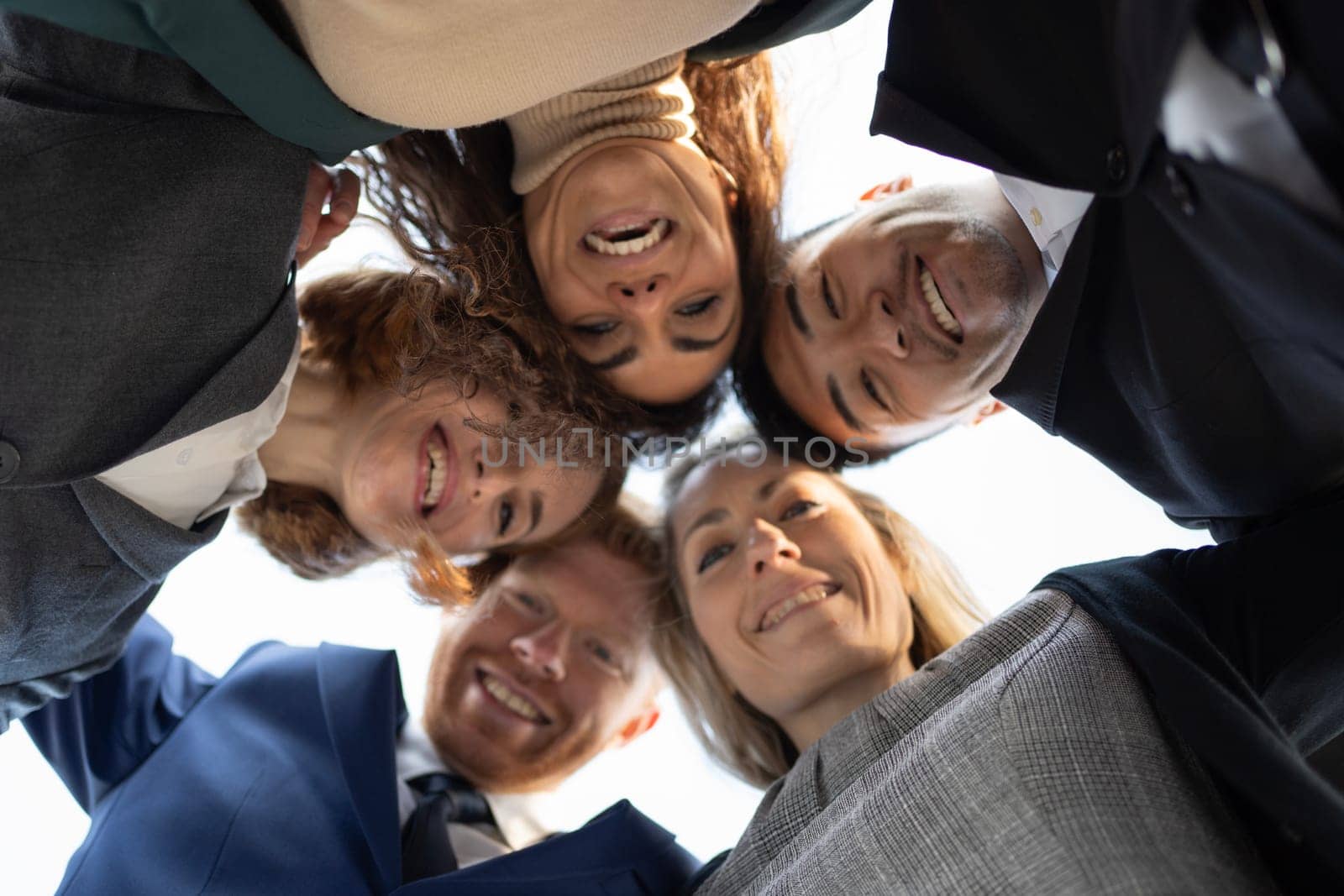 Portrait close up bottom view happy faces of diverse business employees team standing in circle looking at camera.