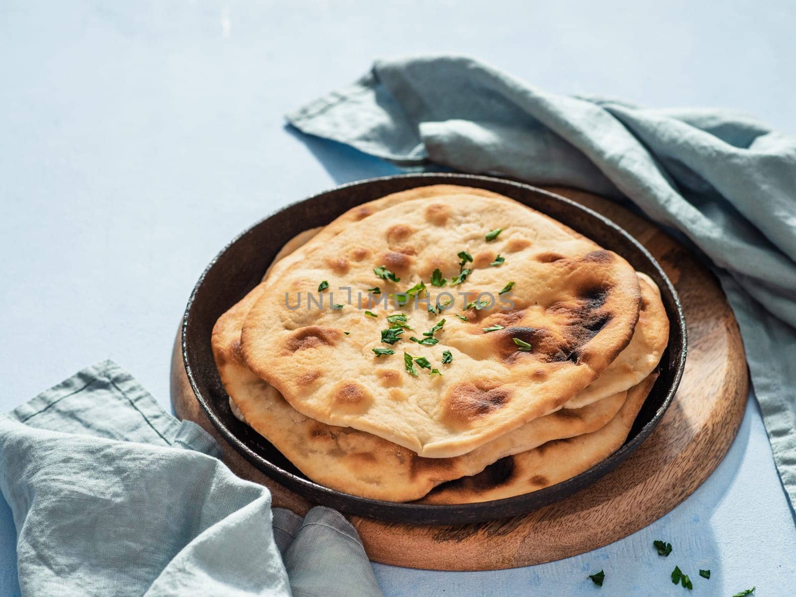 Stack of fesh naan breads in cast-iron pan on blue background with copy space. Perfect naan flatbreads in black circle cast iron pan