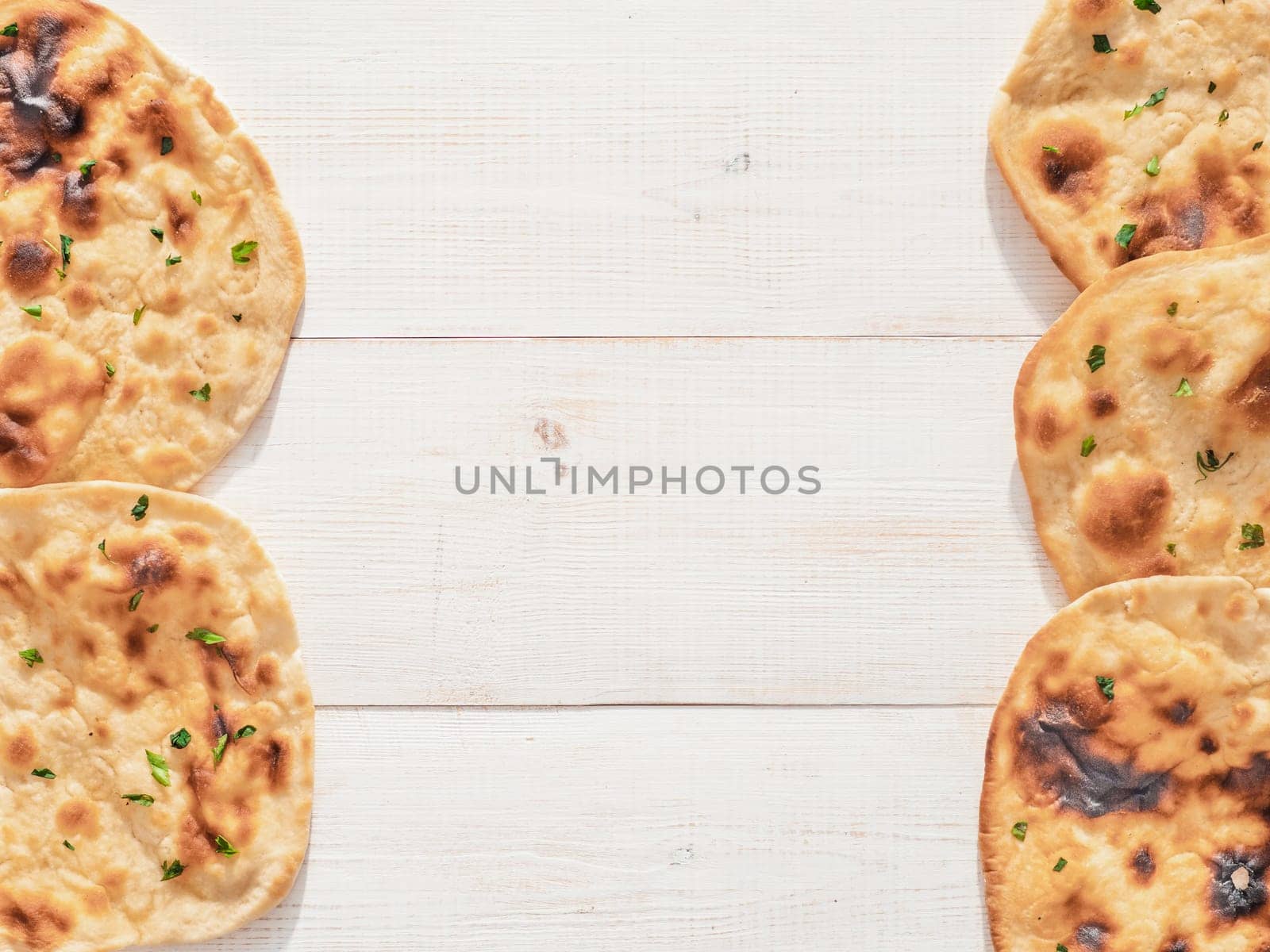 Pattern of fesh naan bread on white wood background with copy space in center. Top view of perfect naan flatbreads as indian pakistani food background