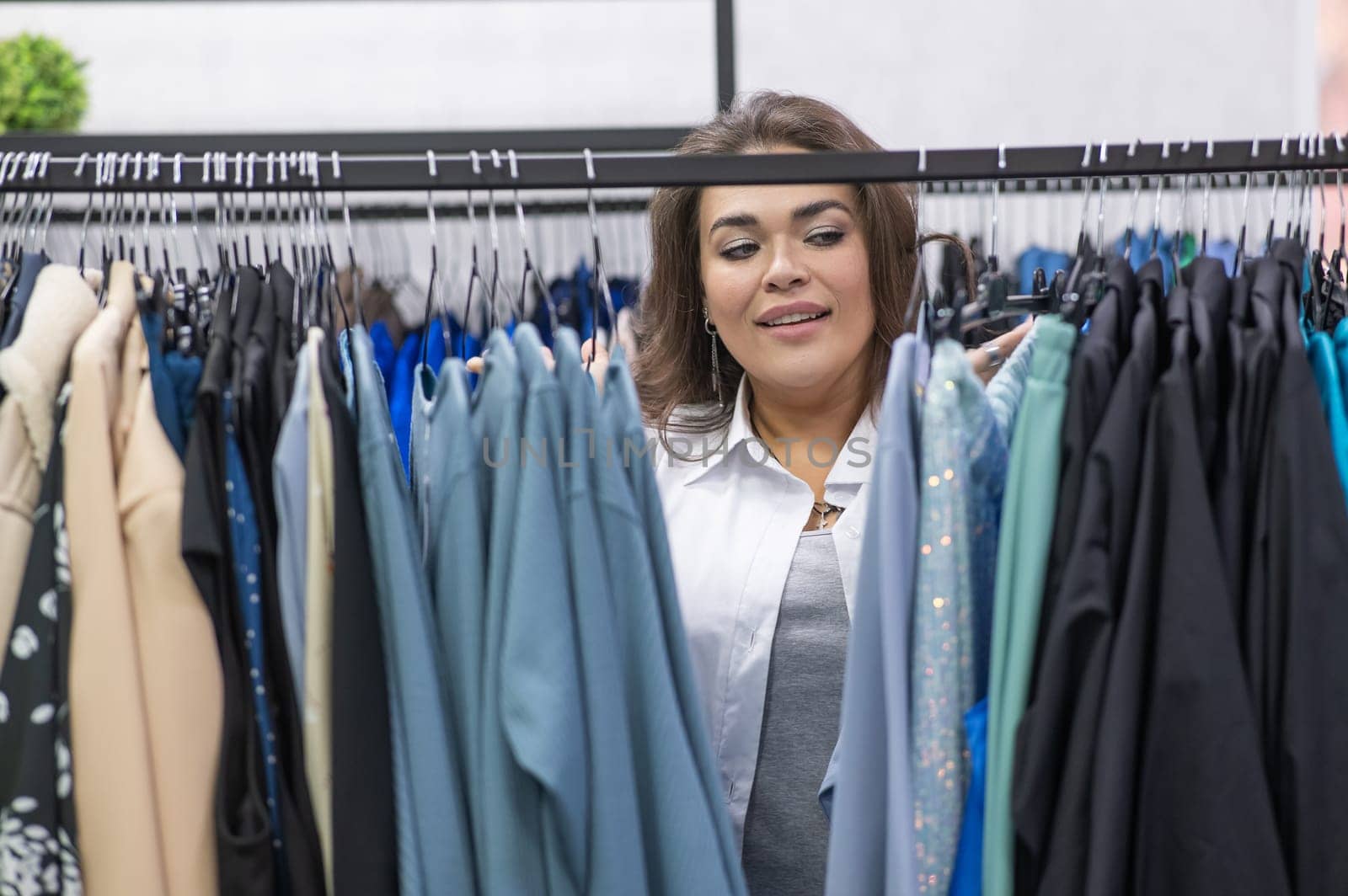 Portrait of a fat woman in a plus size store through hangers with clothes