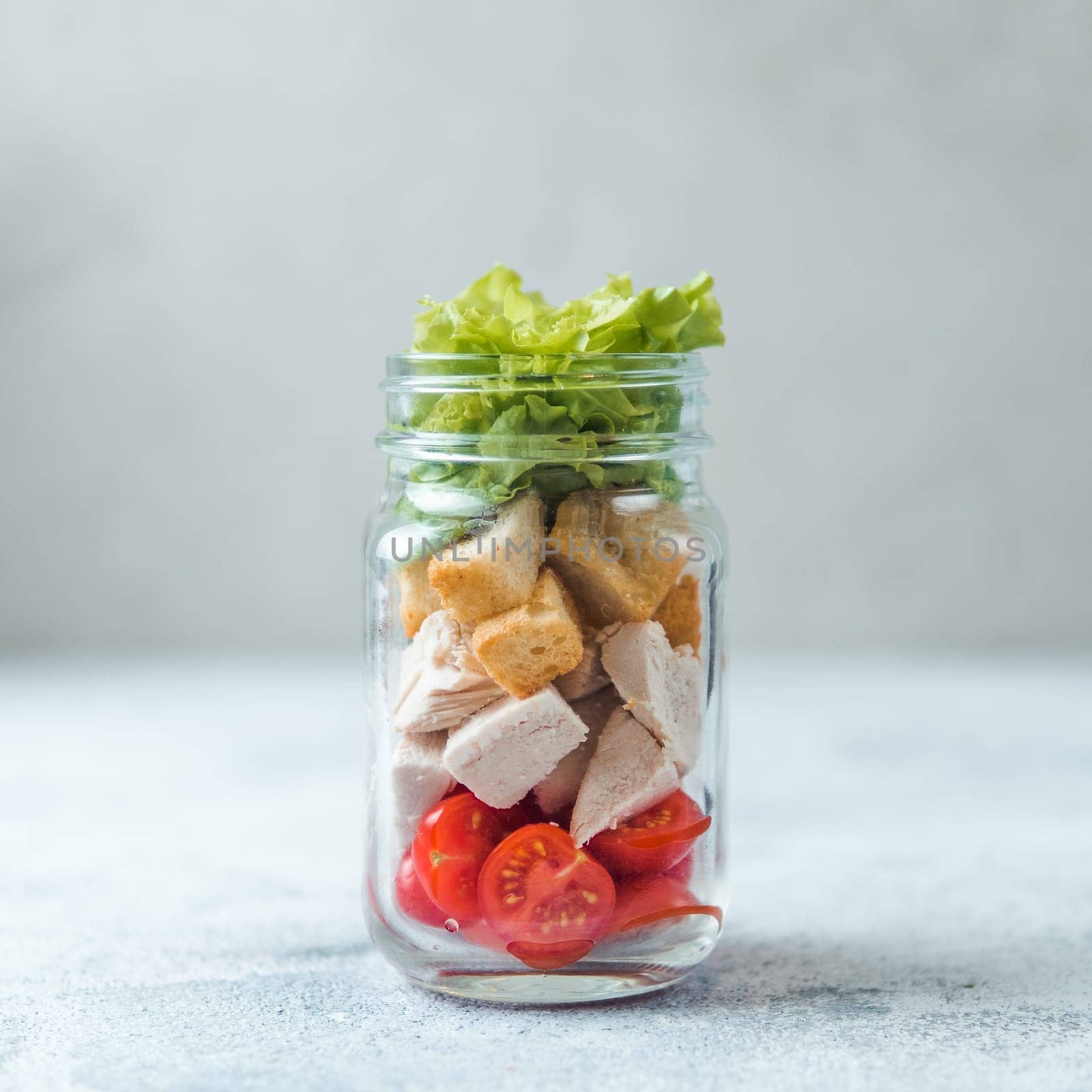 Caesar salad in glass mason jar on gray background. Copy space for text. Homemade healthy caesar salad layered in jar. Healthy food, trendy modern food, diet concept, idea, recipe.