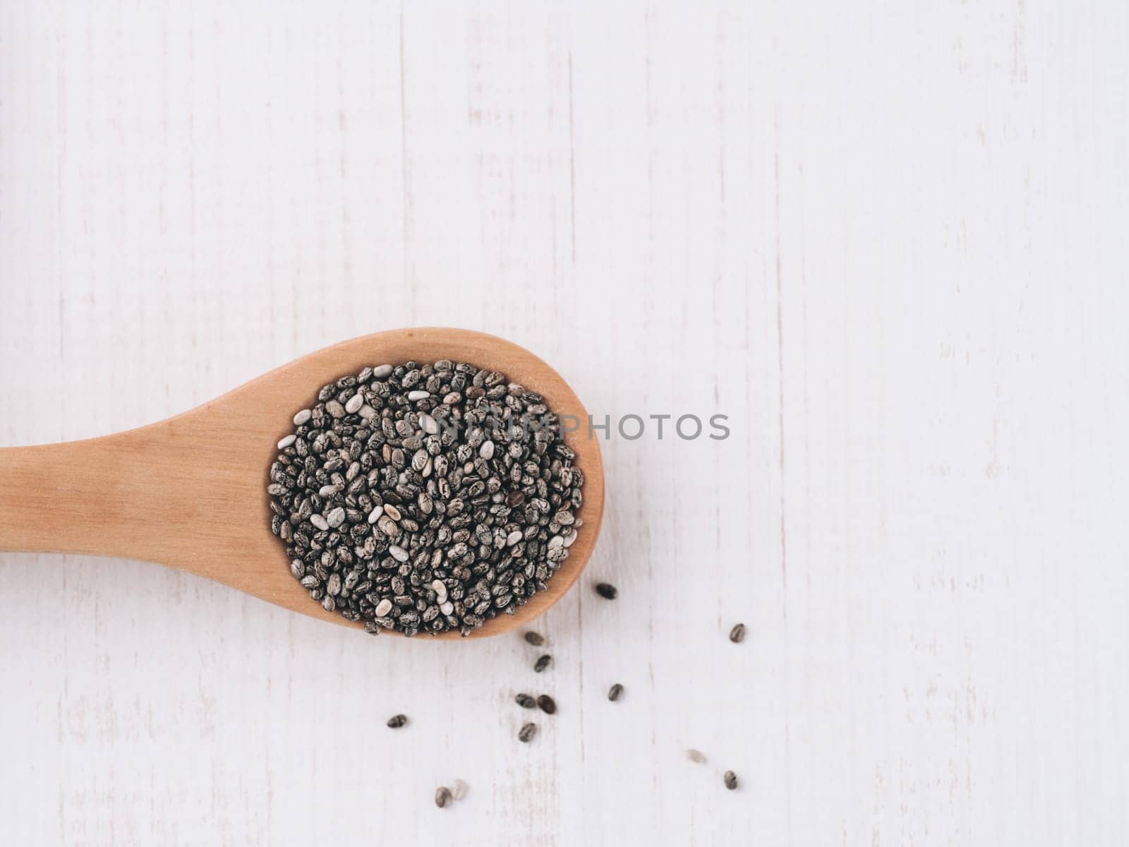 Dry chia seeds in wooden spoons on white wooden background. Cia seeds is superfood ingredient. Copy space for text.