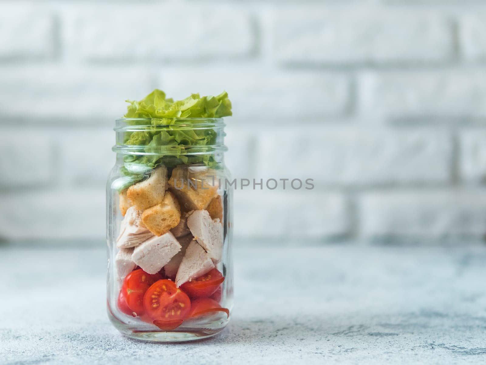 Caesar salad in glass mason jar on gray background. Copy space for text. Homemade healthy caesar salad layered in jar. Healthy food, trendy modern food, diet concept, idea, recipe.