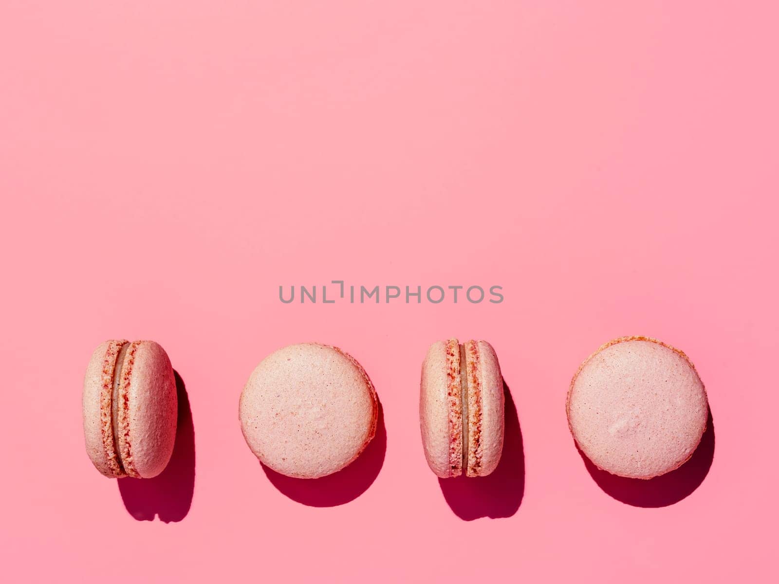 Pink macarons with copy space. Row of perfect french macarons or macaroons on pink background. Top view or flat lay. Hard light