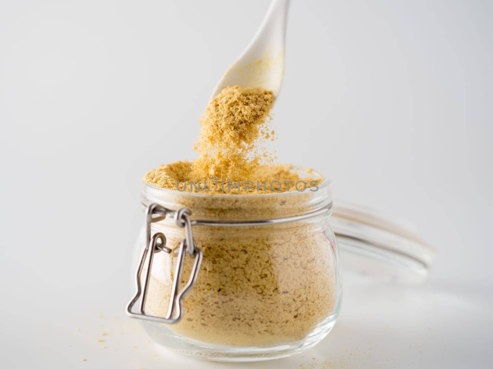 Nutritional yeast background. Nutritional inactive yeast falling from spoon in glass jar on white background. Copy space. Nutritional yeast is vegetarian superfood with cheese flavor, for healthy diet