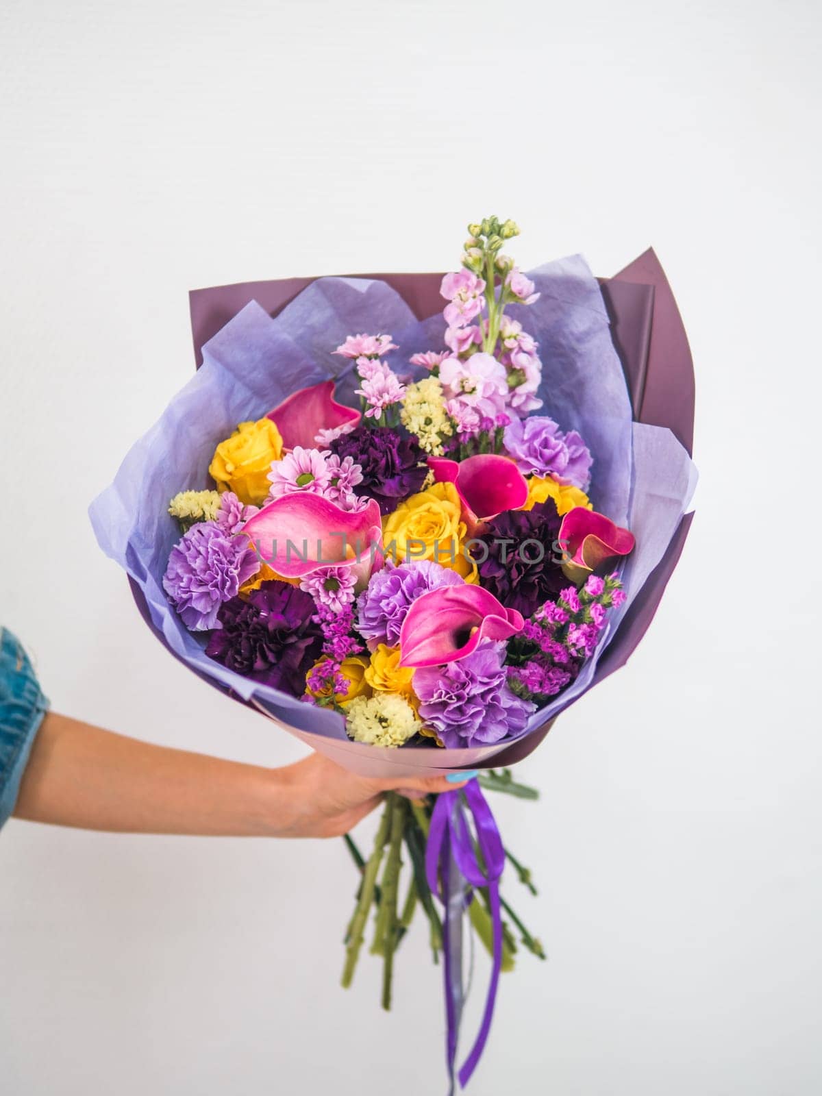 Beautiful bouquet with different flowers in woman hand. Lilac bouquet with arum lily or calla, roses, dianthus, chrysanthemum, limonium, matthiola. Shallow DOF, copy space. Vertical