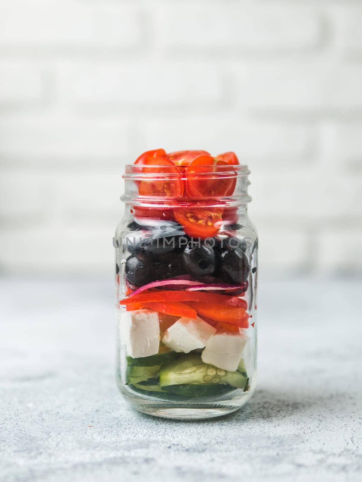 Greek Salad layered in glass mason jar on gray background, copy space. Trendy food. Idea, recept and concept of modern healthy food.