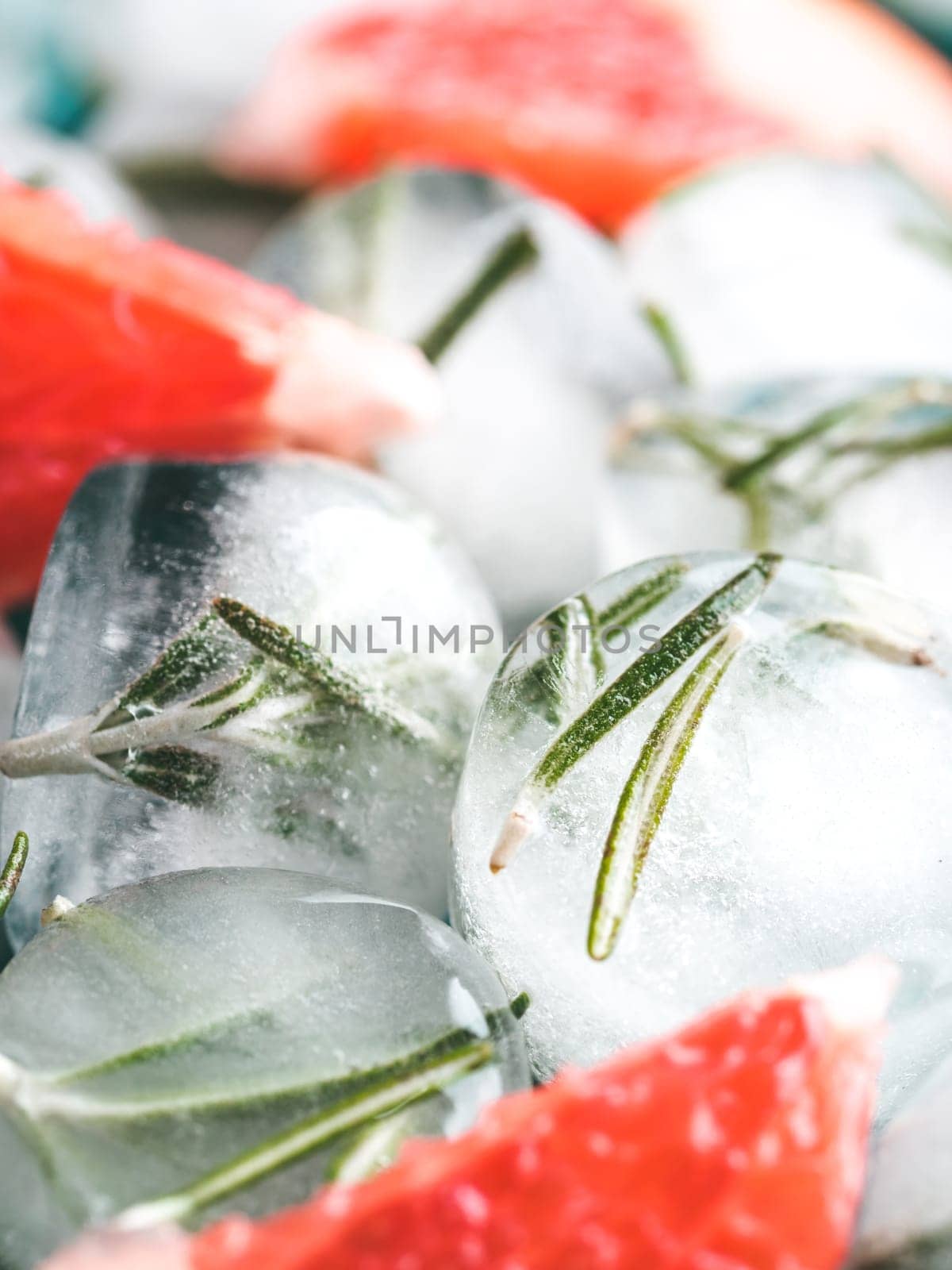 Close up view of detox rosemary ice cubes and fresh rosemary slice over green cement background.