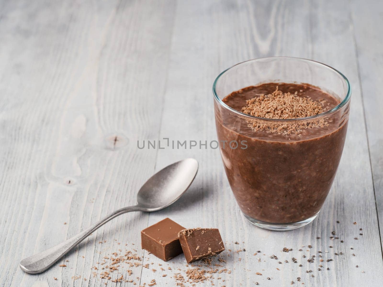 Chocolate chia pudding in glass and chocolate cubes slice on gray wooden table. Healthy vegan breakfast with copy space.