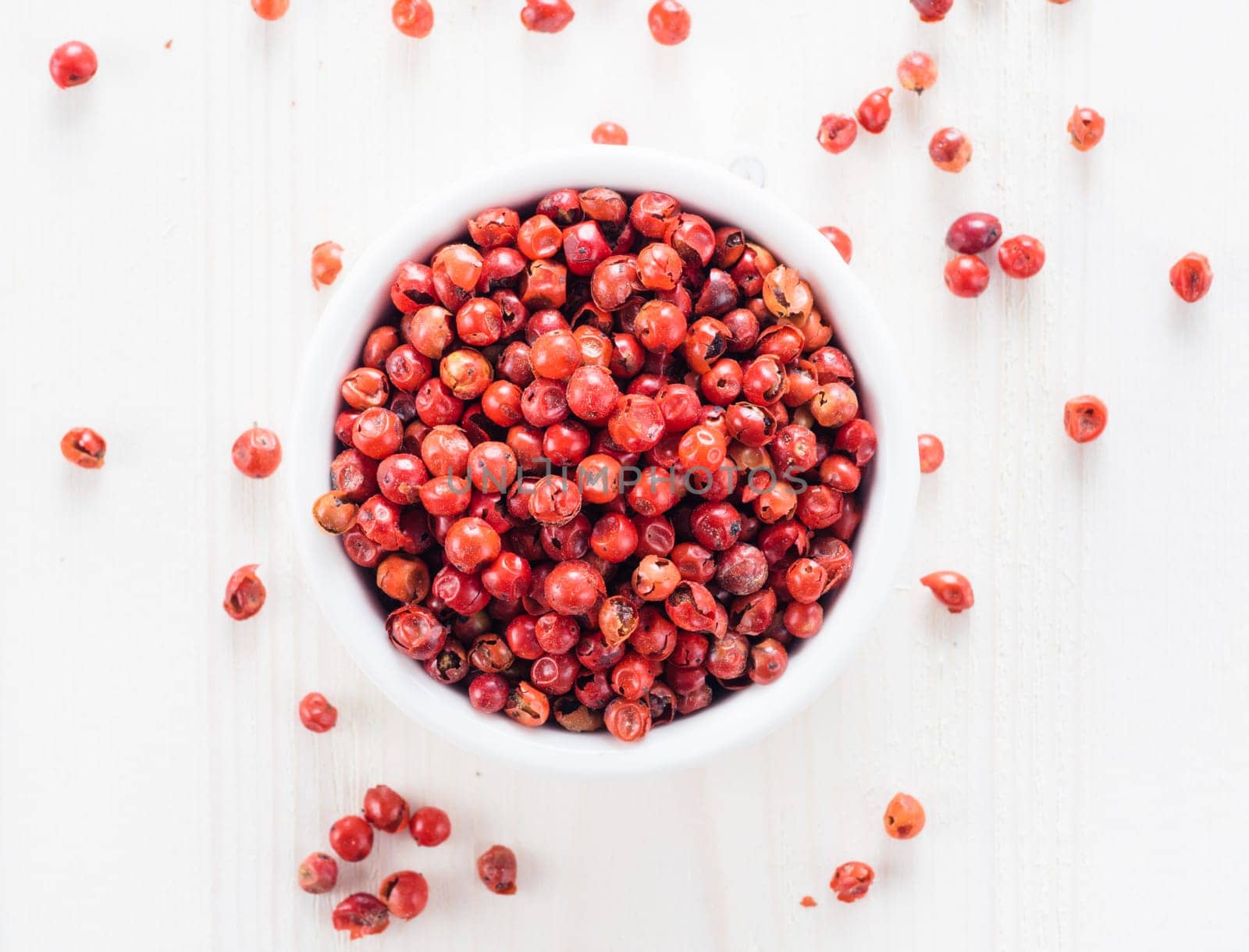 Pile with dried pink pepper berries on white wooden table. Close up view of pink peppercorn. Top view or flat-lay.