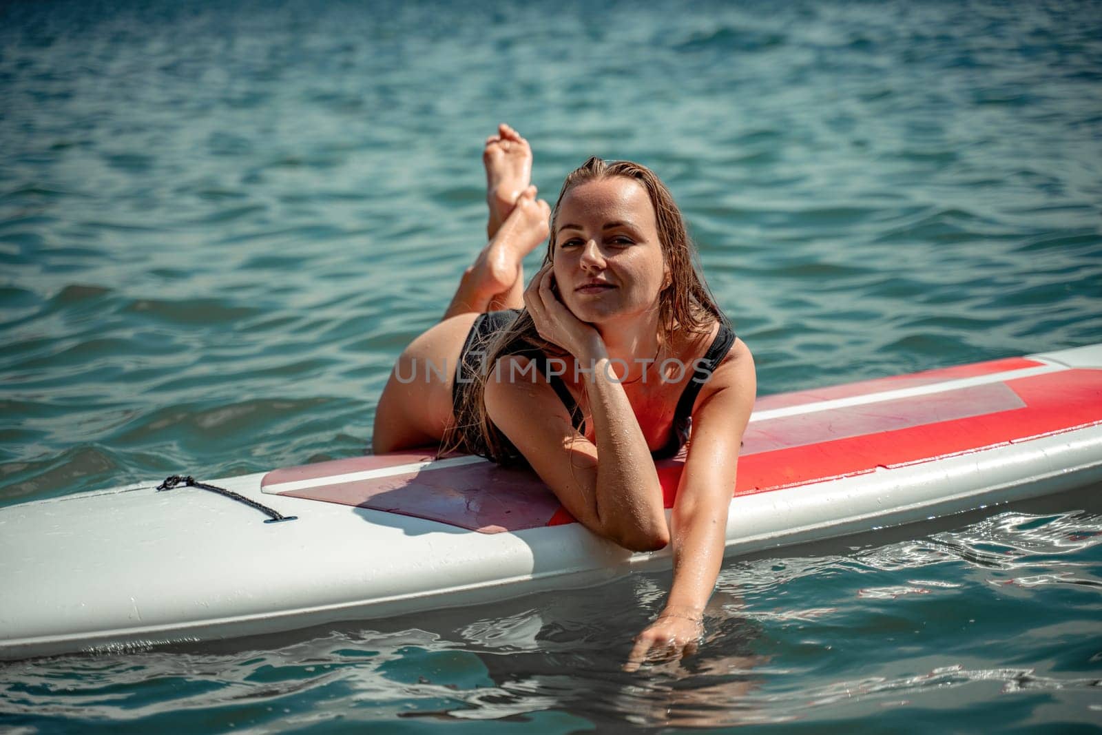 Woman sap sea. Sports girl on a surfboard in the sea on a sunny summer day. In a black bathing suit, he lies on a sap in the sea. Rest on the sea. by Matiunina
