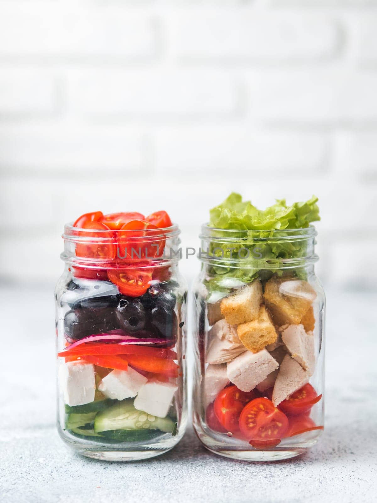 Greek Salad and Caesar salad in glass mason jar on gray background.Homemade healthy caesar salad and greek salad layered in jars.Healthy food, trendy modern food, diet concept, idea, recipe.Copy space