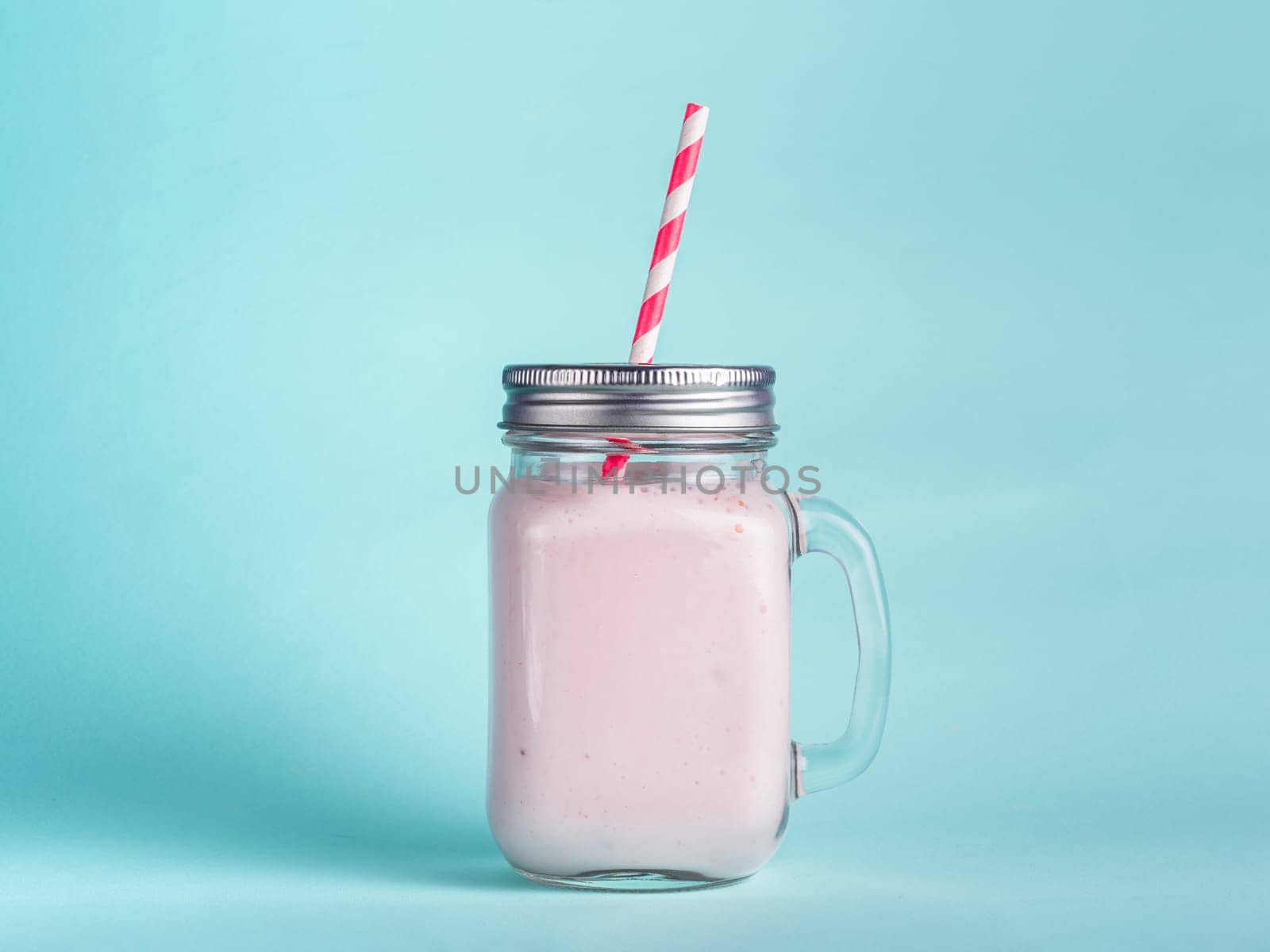 Pink strawberry smoothie in mason jar glass. Isolated on blue background.