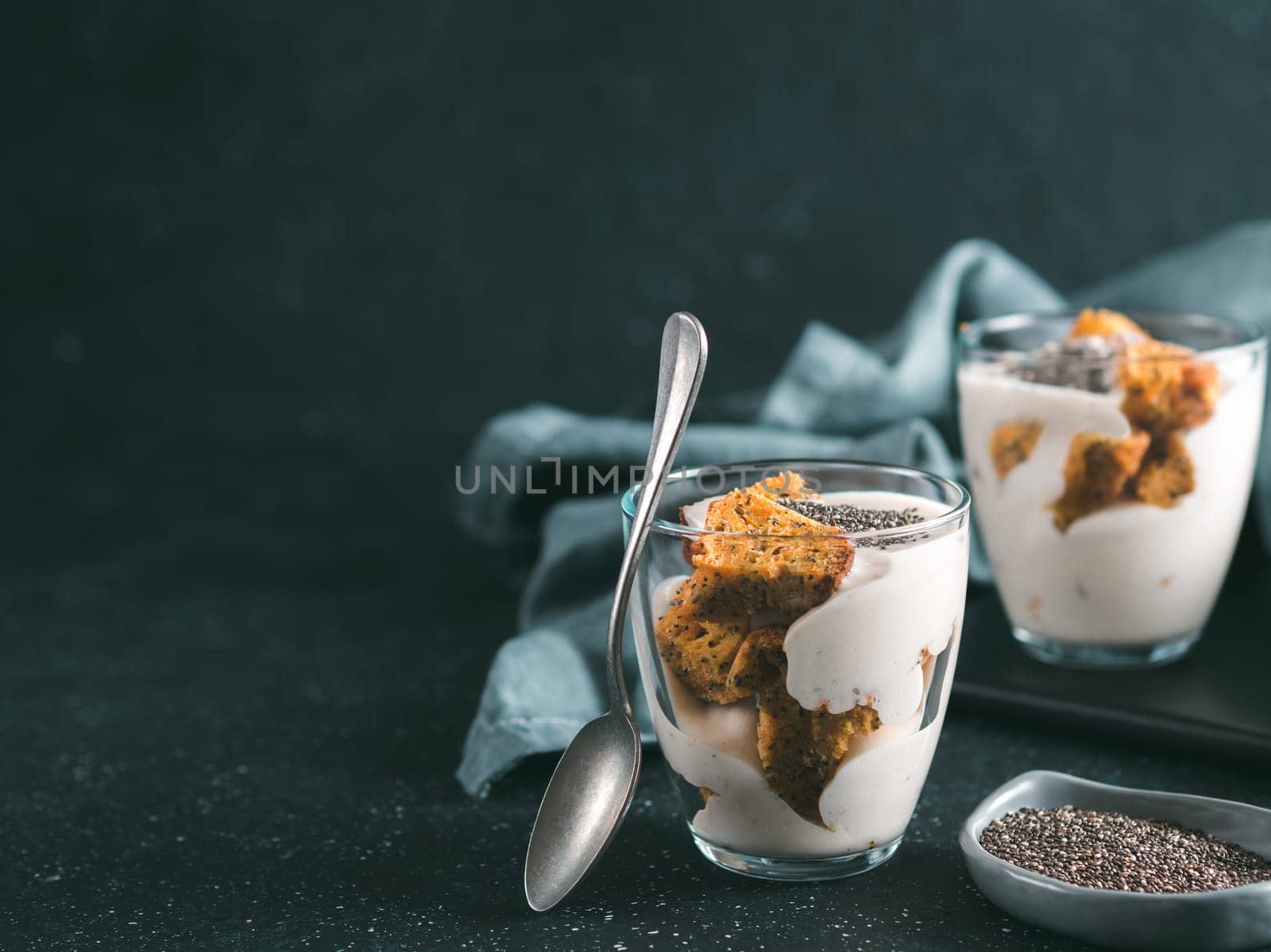 No baked cheesecake dessert with crushed carrots biscuits and chia seeds in glass jar on dark background. Ideas and recipes for healthy breakfast. Copy space for text.