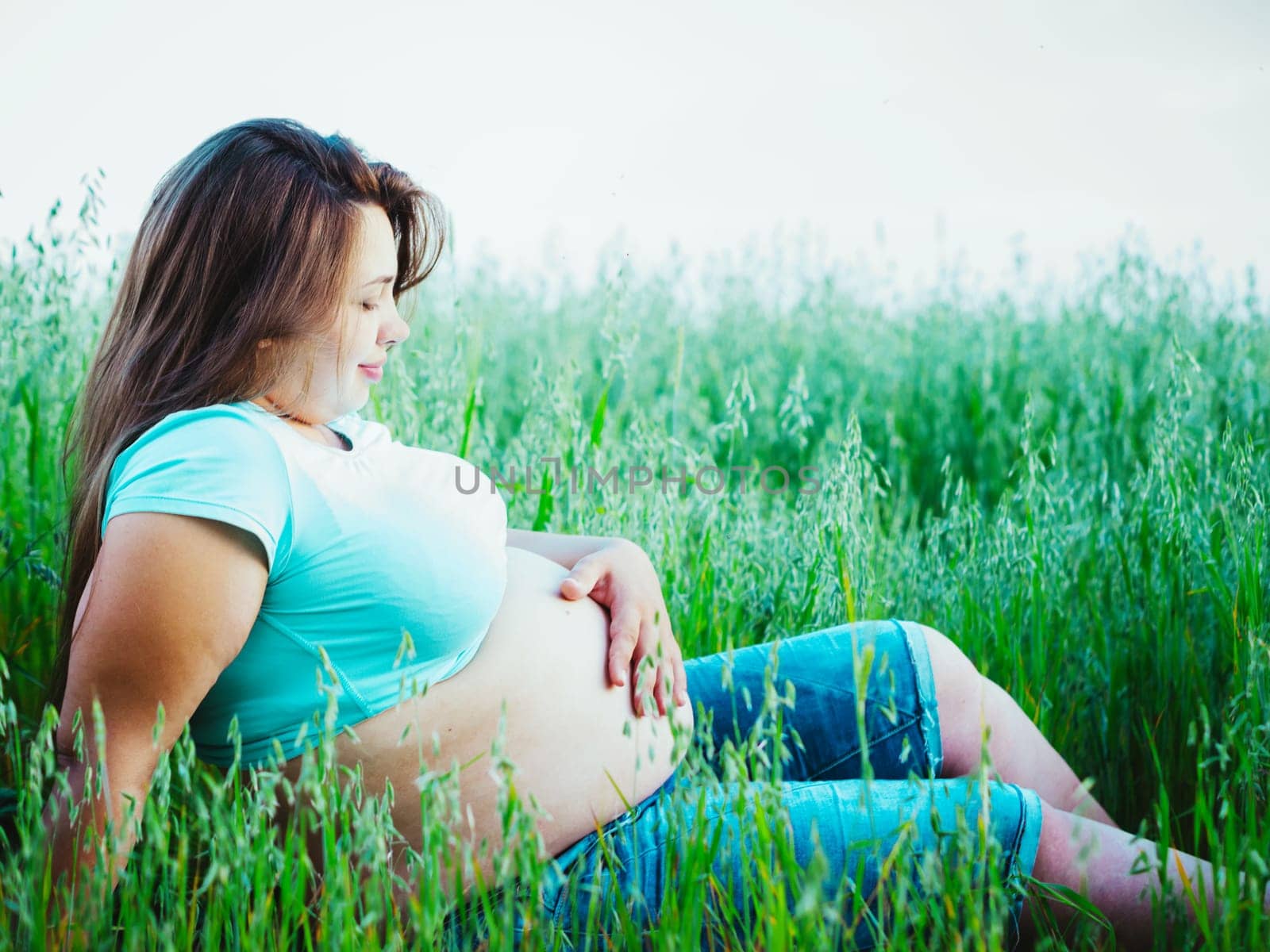 Pregnant woman sitting and looking at her belly outdoors by fascinadora