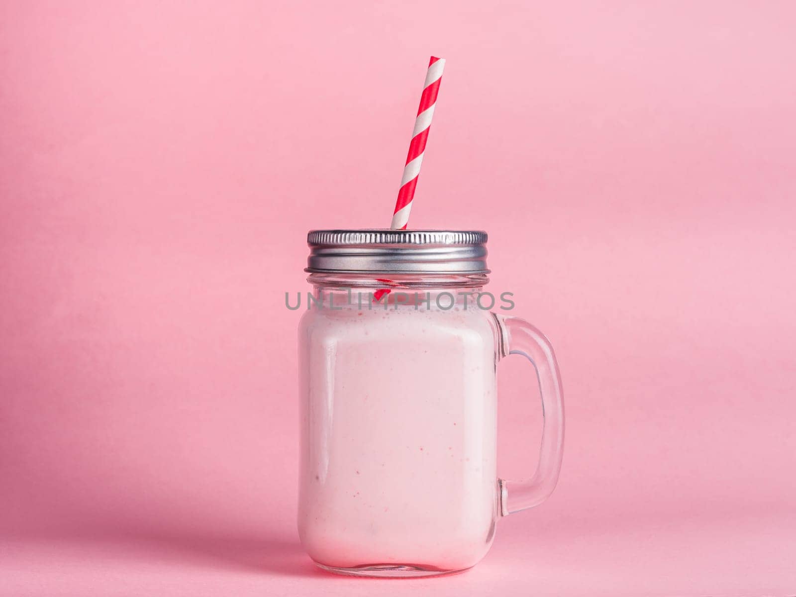 Pink strawberry smoothie in mason jar glass on pink background