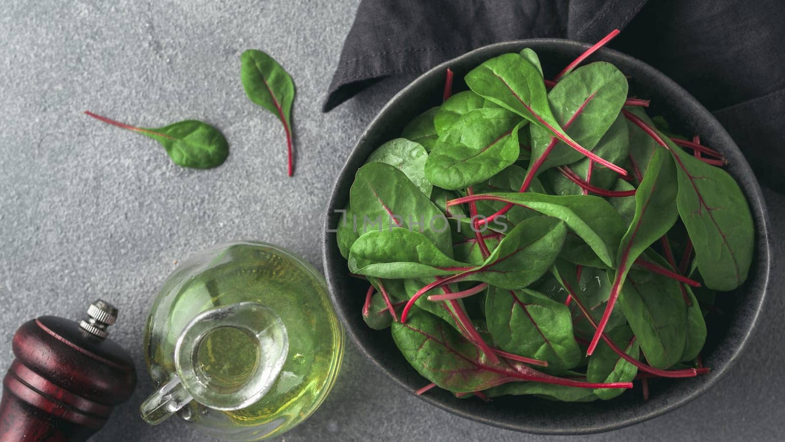 Fresh salad of green chard leaves or mangold on gray stone background. Flat lay or top view fresh baby beet leaves in craft ceramic bowl. Banner for web