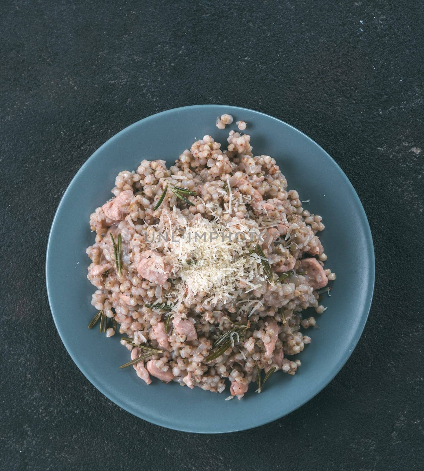 Raw buckwheat risotto with chicken meat and rosemary served parmesan cheese in gray plate on black cement background. Gluten-free and buckwheat recipe ideas. Copy space.
