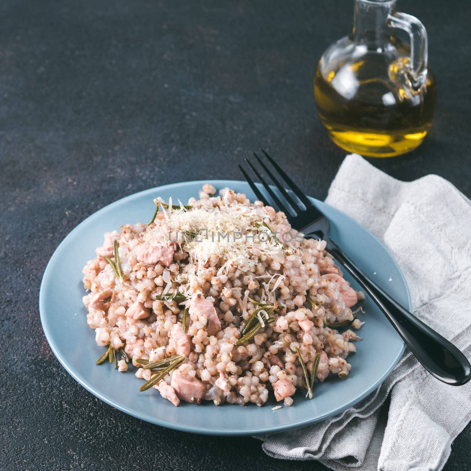 Raw buckwheat risotto with chicken meat and rosemary served parmesan cheese in gray plate on black cement background. Gluten-free and buckwheat recipe ideas. Copy space. Toned image.
