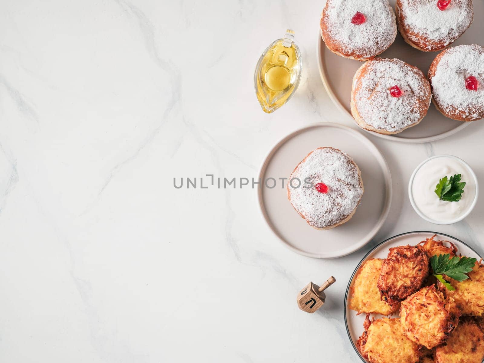 Jewish holiday Hanukkah concept and background. Hanukkah food doughnuts and potatoes pancakes latkes, oil and traditional spinnig dreidl. on marble table. Top view or flat lay. Copy space for text.