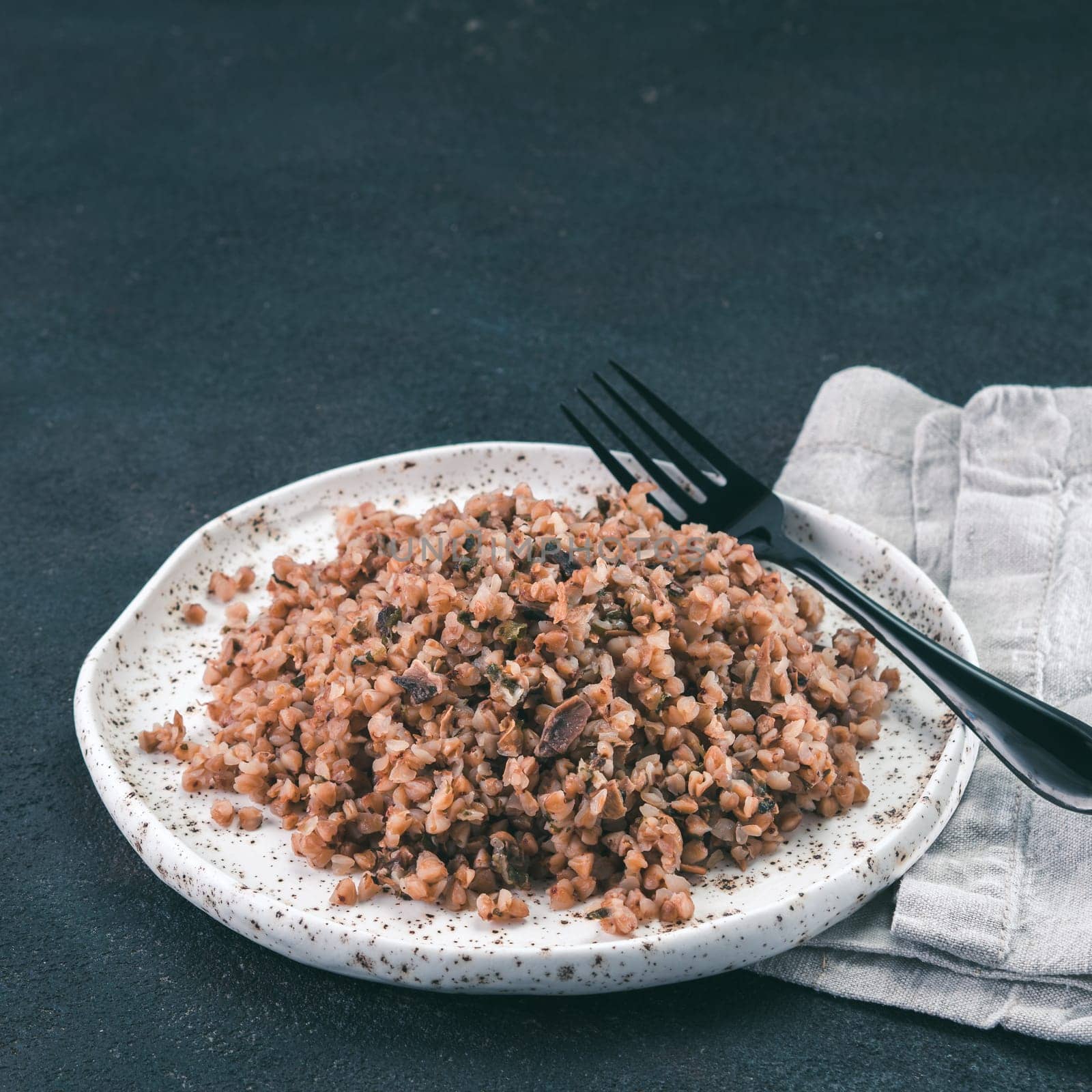 Buckwheat risotto with dried mushrooms in craft plate on black cement background. Gluten-free and vegetarian buckwheat recipe ideas. Copy space. Toned image Toned image.