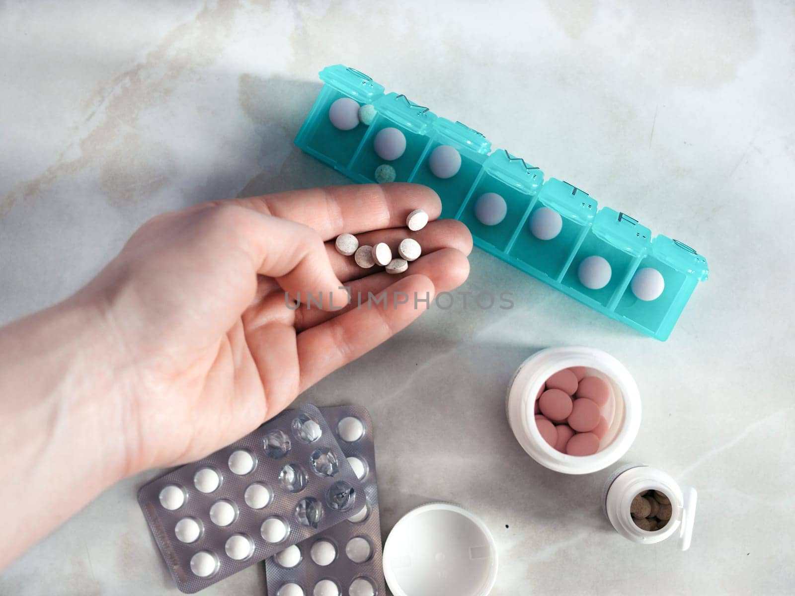 Hand with pills and pillbox. Top view of seven day pill box with pills. Green pill-box over light marble table. Open pill box and open boxes with pills or vitamins. Copy space. Top view or flat-lay.