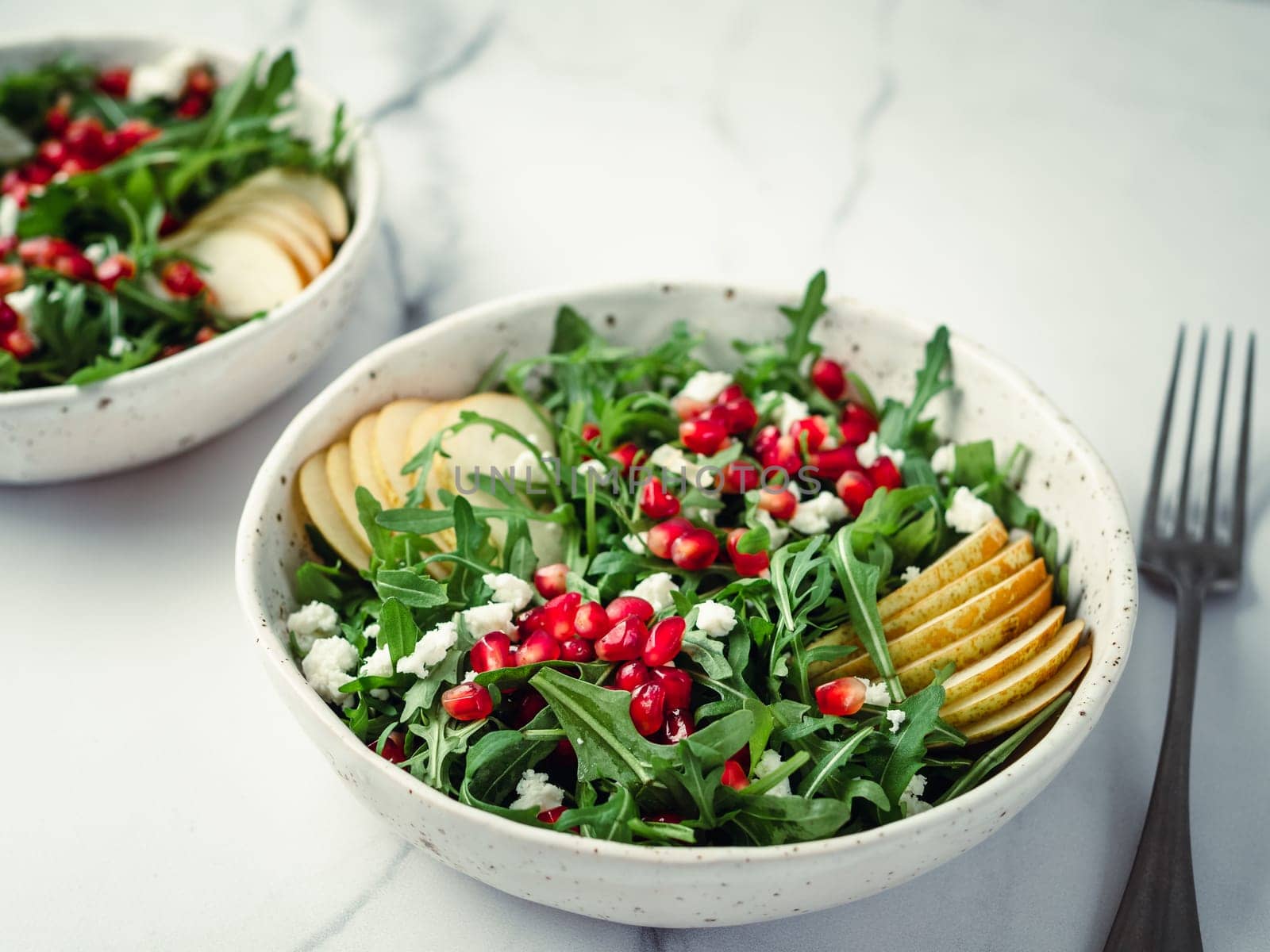 Fresh salad with arugula, pear, pomegranate and coconut crumble or cottage cheese. Two bowls with delicious summer fruit salad on marble table. Copy space for text