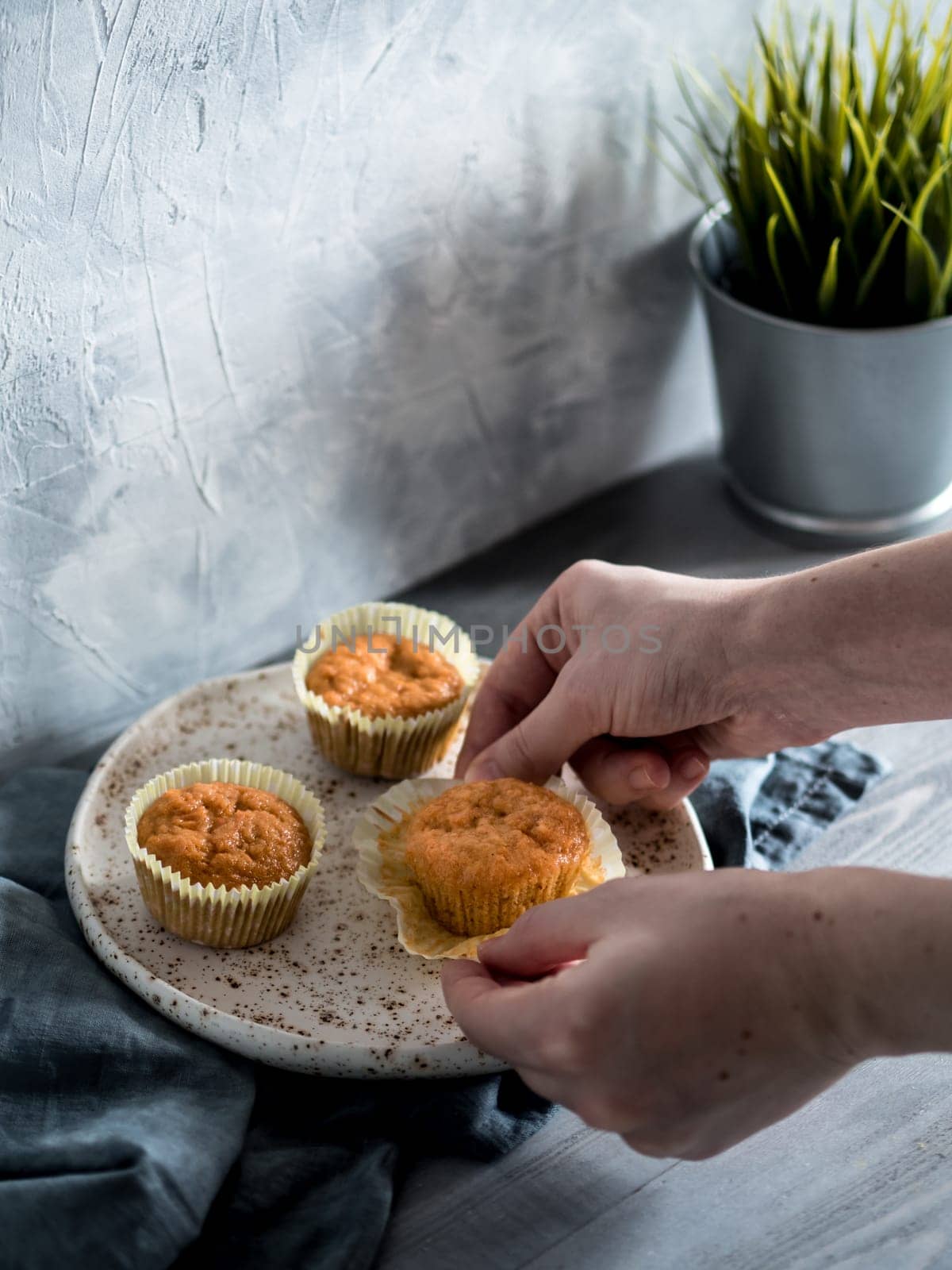 Homemade muffins on craft plate over gray wooden table. Hands hold carrot cupcake. Copy space. Toned image in scandinavian style.