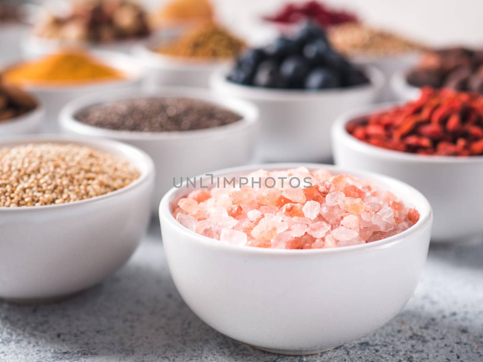 Pink salt in small white bowl and other superfoods on background. Selective focus. Different superfoods ingredients. Concept and illustration for superfood and detox food