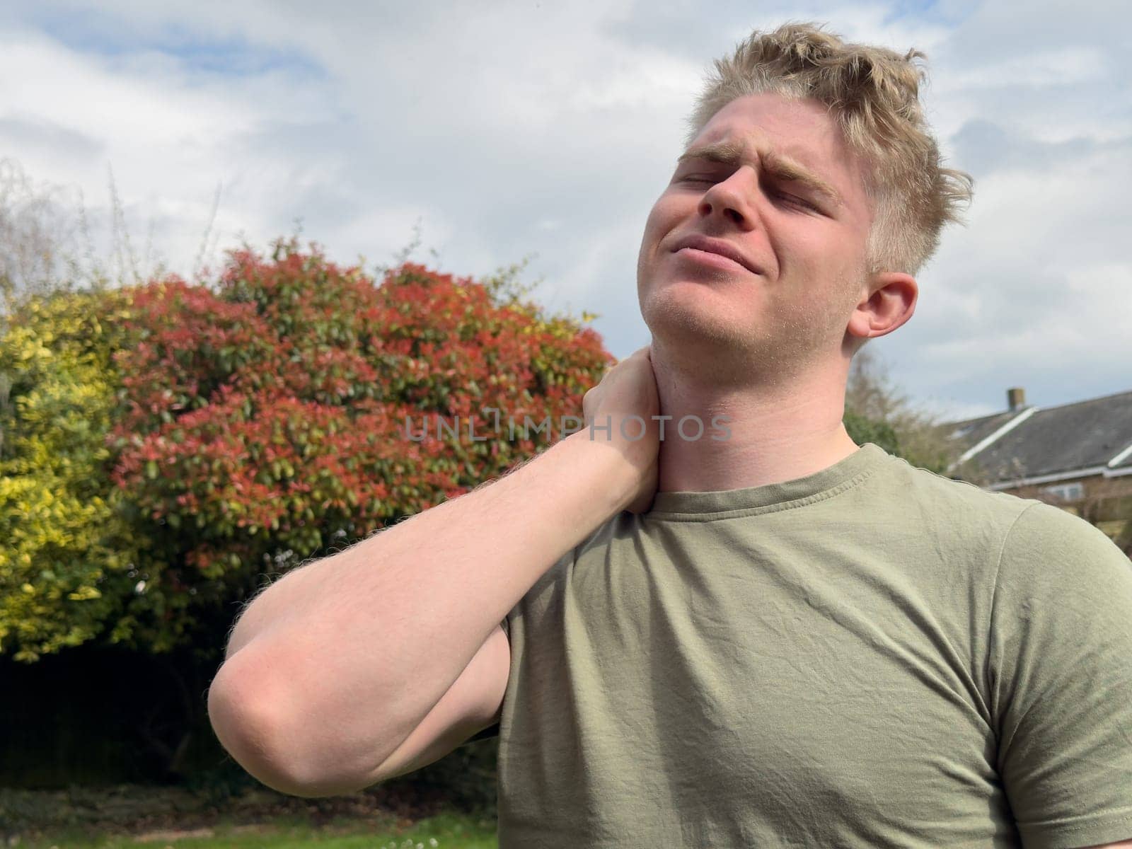 Young man massaging his aching neck standing outdoors