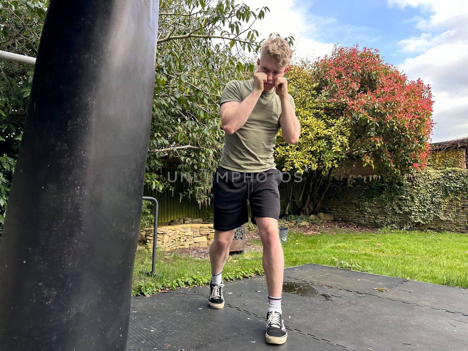 Young handsome male fighter exercising outdoors with a punching bag