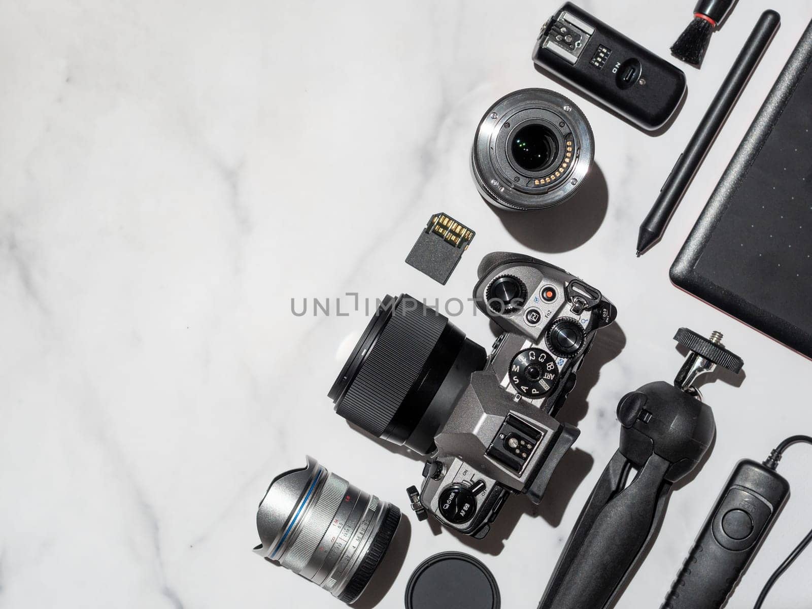 Photographer workplace with dslr camera, lens, pen tablet and camera accessorieson white marble background. Camera, photography, visual content concept. Flat lay or top view. Copy space. Hard light.