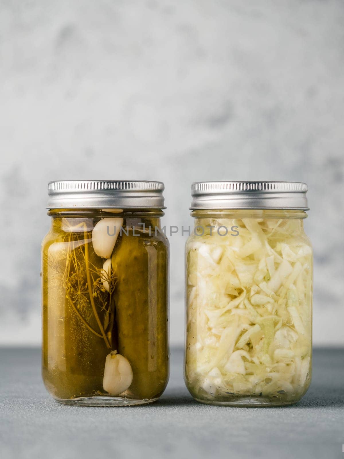 Pickled cucumbers and Sauerkraut on gray background with copy space for text. Perfect homemade marinated cucumbers and pickling cabbage in mason jar at home on table. Vertical