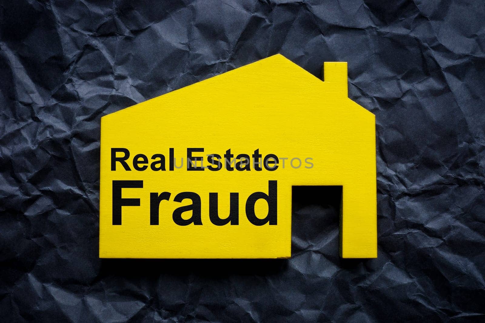 Crumpled black paper and house with inscription Real estate fraud. by designer491