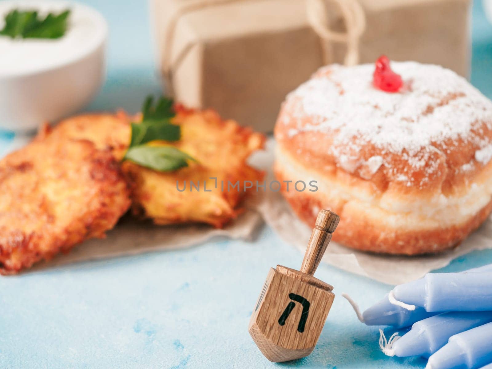 Jewish holiday Hanukkah concept and background. Hanukkah food doughnuts and potatoes pancakes latkes, giftbox, candle and traditional spinnig dreidl on blue background. Copy space for text.