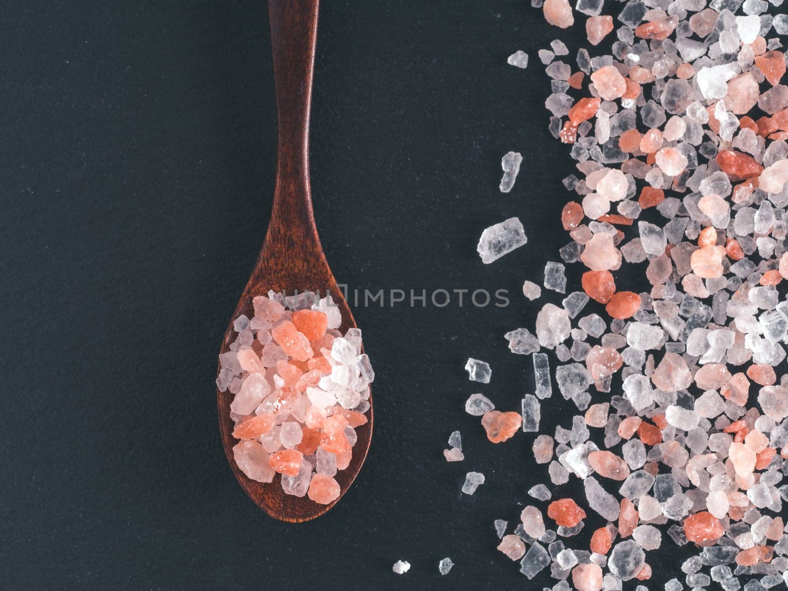 Himalayan pink salt in spoon on black stone background. Copy space