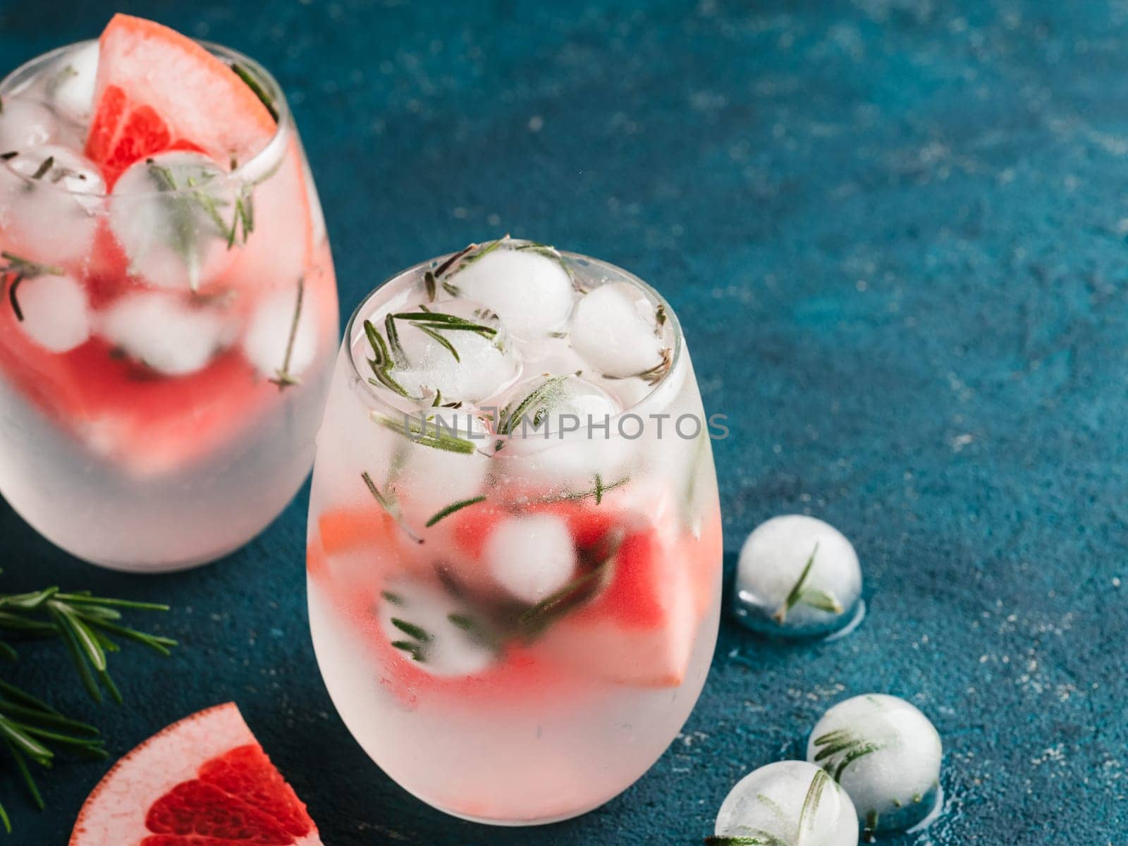 infused detox water or alcoholic or non-alcoholic cocktail with grapefruit and rosemary ice in glass on green cement background. healthy eating or holyday drink concept, copy space for text.