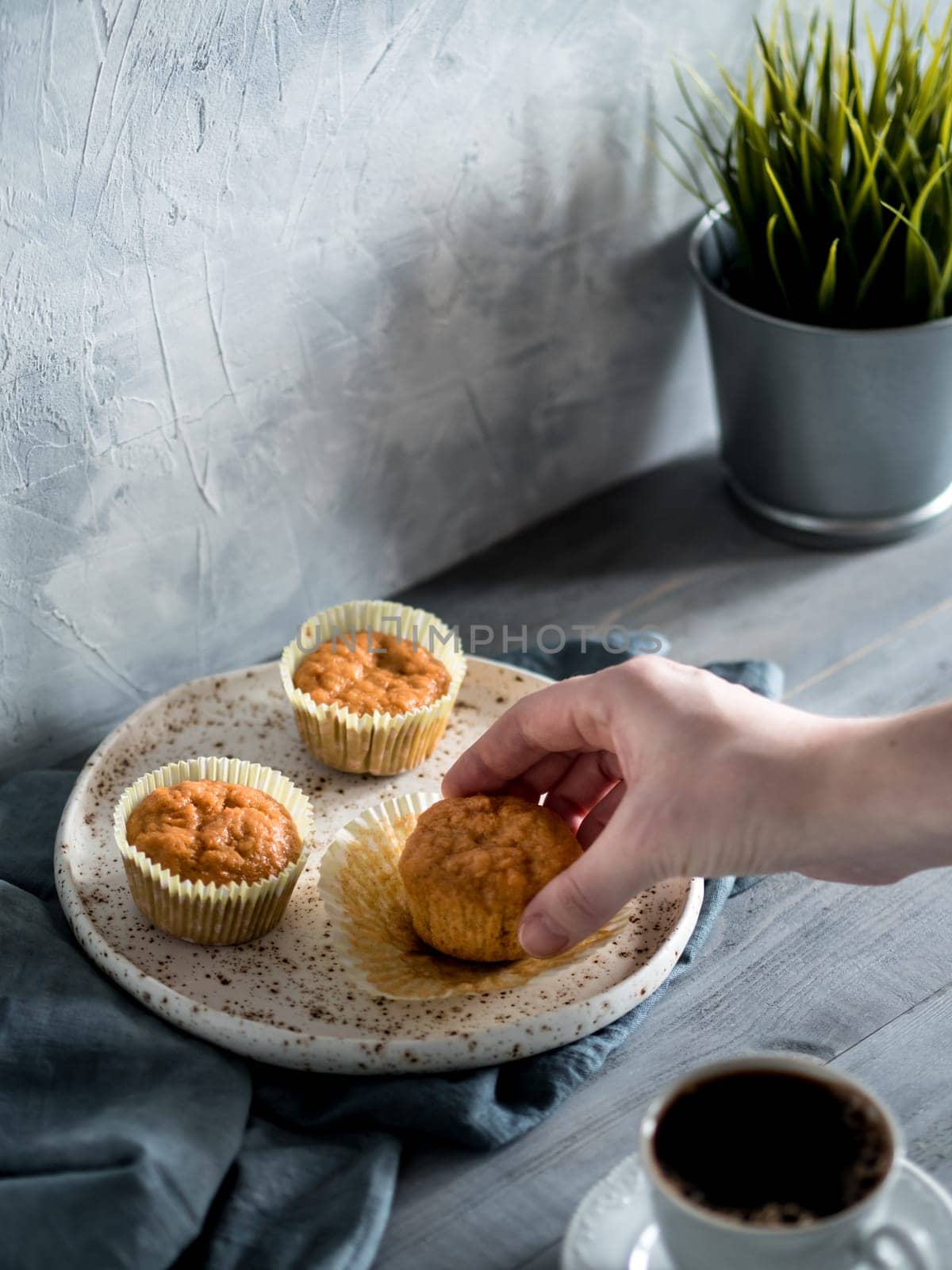 Homemade muffins on craft plate over gray wooden table. Hand hold carrot cupcake. Copy space. Toned image in scandinavian style.