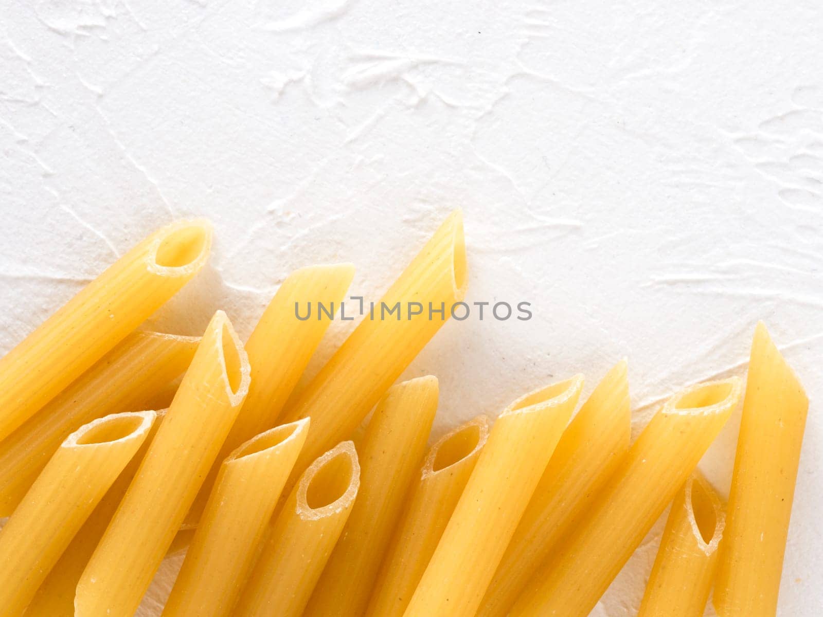 raw pasta penne on white background by fascinadora