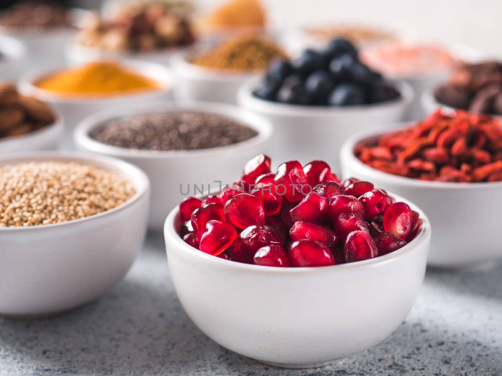 pomegranate or grain of garnet in small white bowl and other superfoods on background. Selective focus. Different superfoods ingredients. Concept and illustration for superfood and detox food