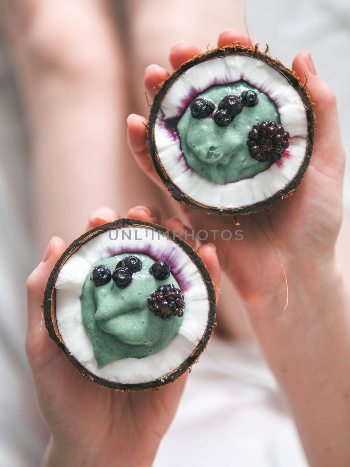 Two coconut half with smoothie or yogurt in woman hands. Blue spirulina smoothie in coconut with frozen berries. Healthy breakfast concept. Ideas and recipes for healthy vegan breakfast. Copy space