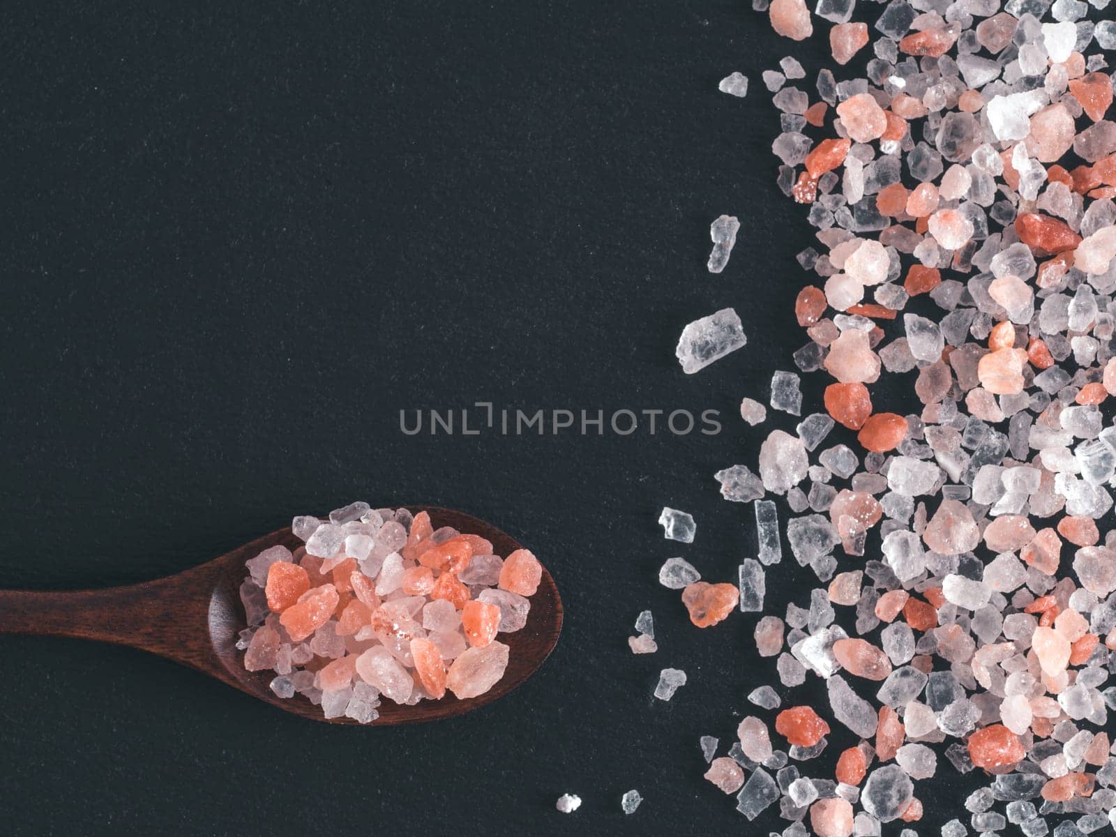 Himalayan pink salt in spoon on black stone background. Copy space