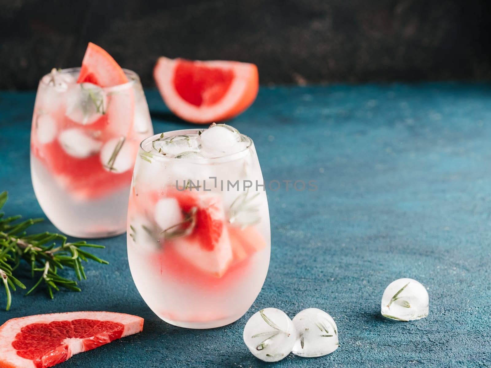 infused detox water or alcoholic or non-alcoholic cocktail with grapefruit and rosemary ice in glass on green and black cement background. healthy eating or holyday drink concept, copy space for text