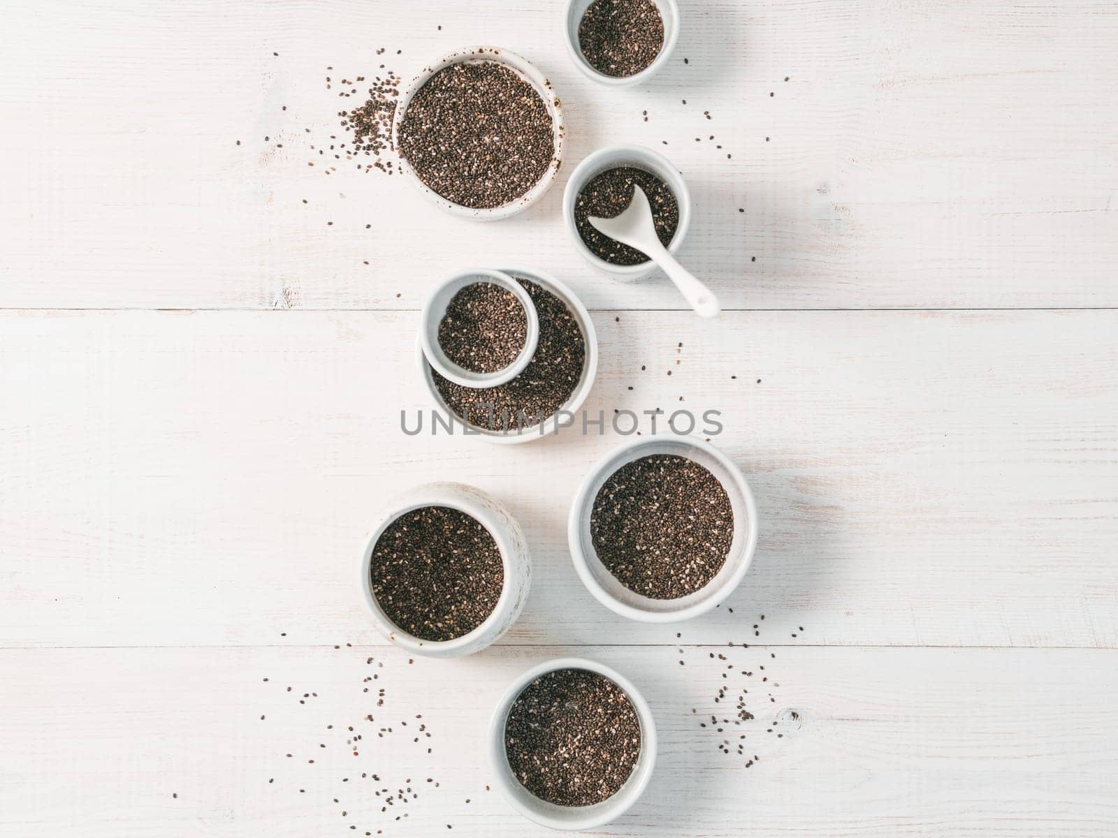 Organic chia seeds on white wooden table. Set of small bowls with organic chia seed. Superfood concept. Copy space. Top view or flat-lay.