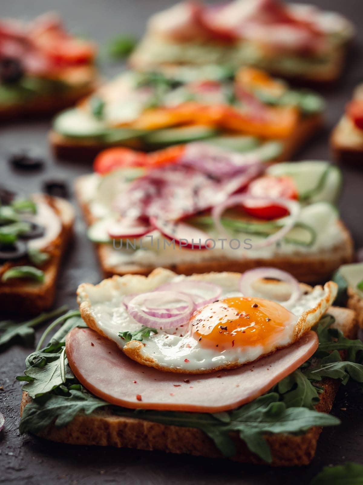 Close up view of different sandwiches with meat, egg, vegetables and herbs. Copy space for text. Assortment meat toasts on black background. Idea, creative concept for sausage maker. Vertical