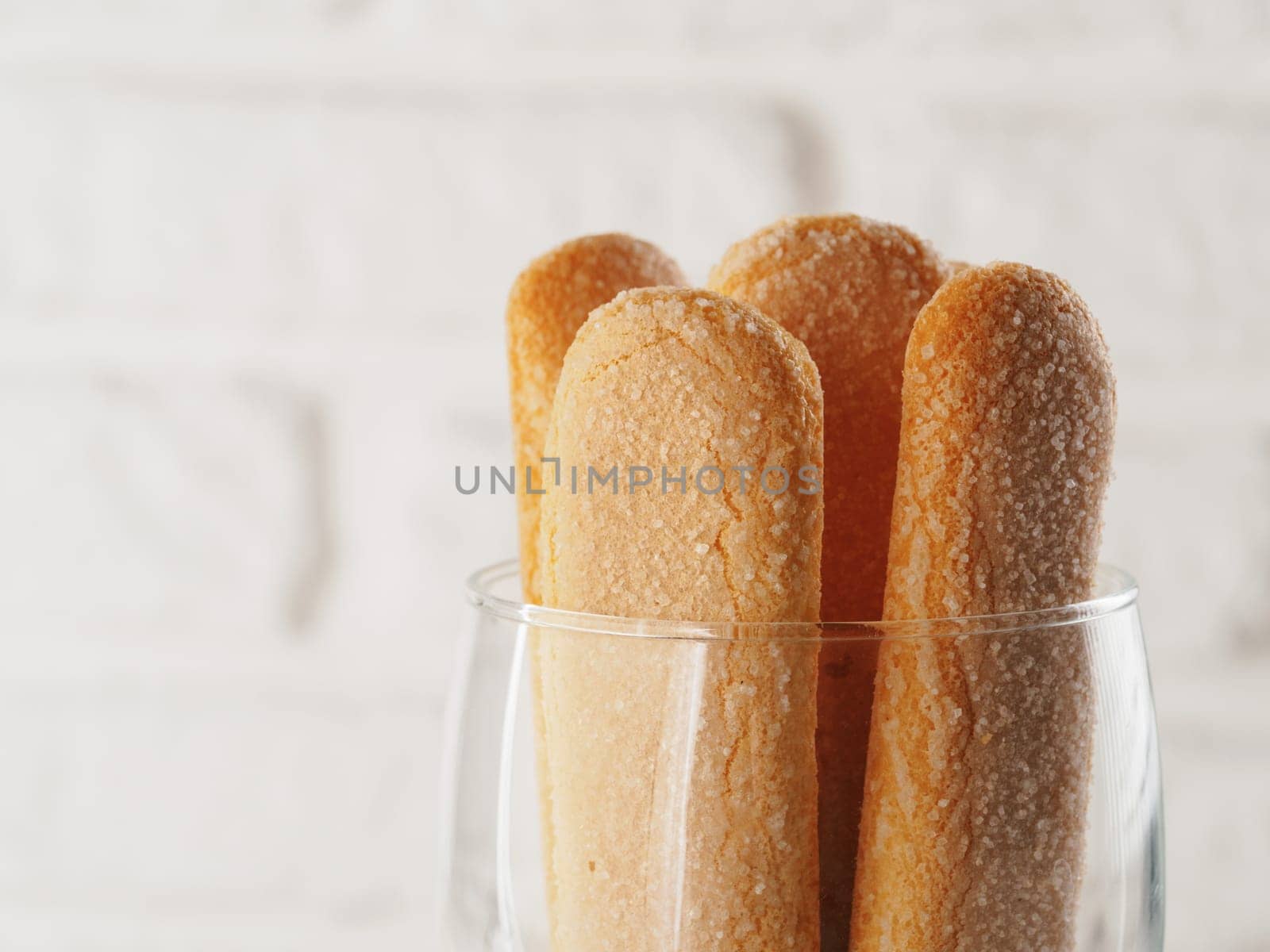 Close up view of ladyfinger biscuit cookie in glass jar on white brick wall background. Italian cookie savoiardi. Copy space.