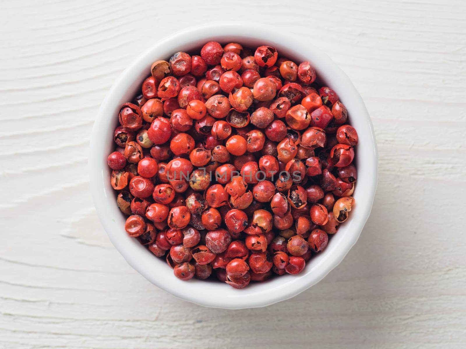 Pile with dried pink pepper berries on white wooden table. Close up view of pink peppercorn. Top view or flat-lay.
